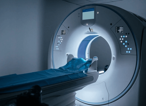 A modern CT scan machine in a dimly lit room, featuring a circular opening and a patient bed covered with a blue sheet.