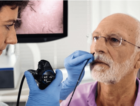 A healthcare professional in blue gloves examines an older man using a medical device, with a monitor displaying an image behind them.